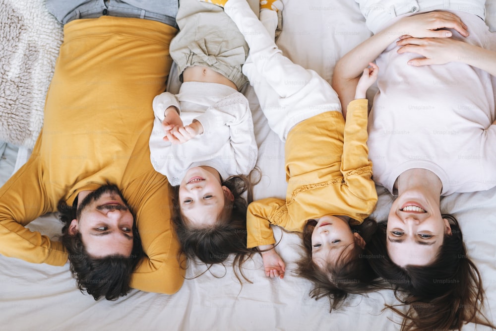 Young happy family with two children girls on bed in cozy home, view from top