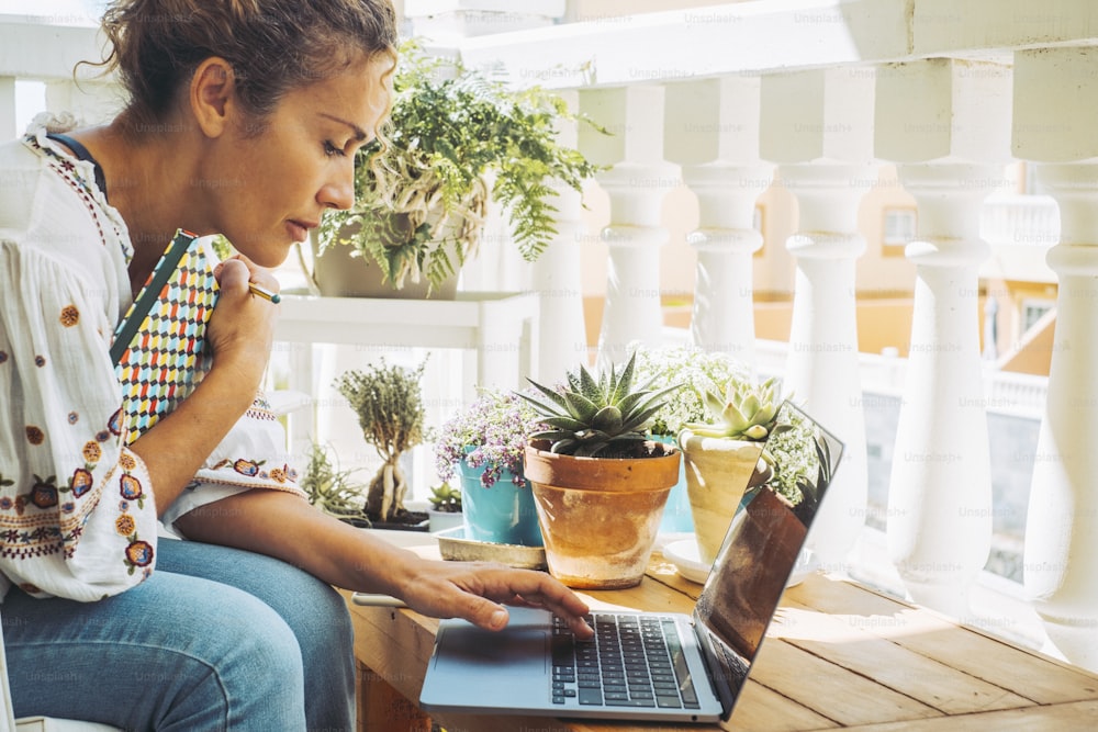 Side portrait of serious business woman working from home in outdoor terrace using laptop. People and computer wireless connection. Concept of online work and digital job lifestyle. Female smart work