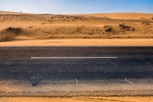 Black asphalt road with sand dunes and desert on left and right and blue sky in background  - travel concept in arid desertic world due a bad climate change future - water emergency planet