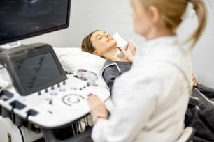 Doctor examining thyroid of female patient with ultrasound scan in medical clinic. Health and wellness concept.