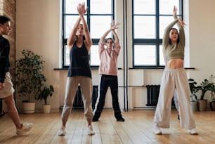 Gruppe von Mädchen im Teenageralter und Jungs, die während der Übung des Vogue-Tanzes bei der Wiederholung im Loft-Studio die Arme über den Kopf heben