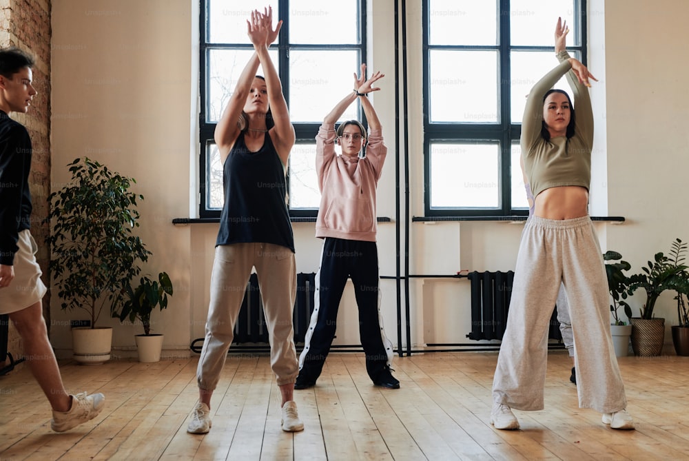 Group of teenage girls and guy raising stretched arms over their heads during exercise of vogue dancing at repetition in loft studio