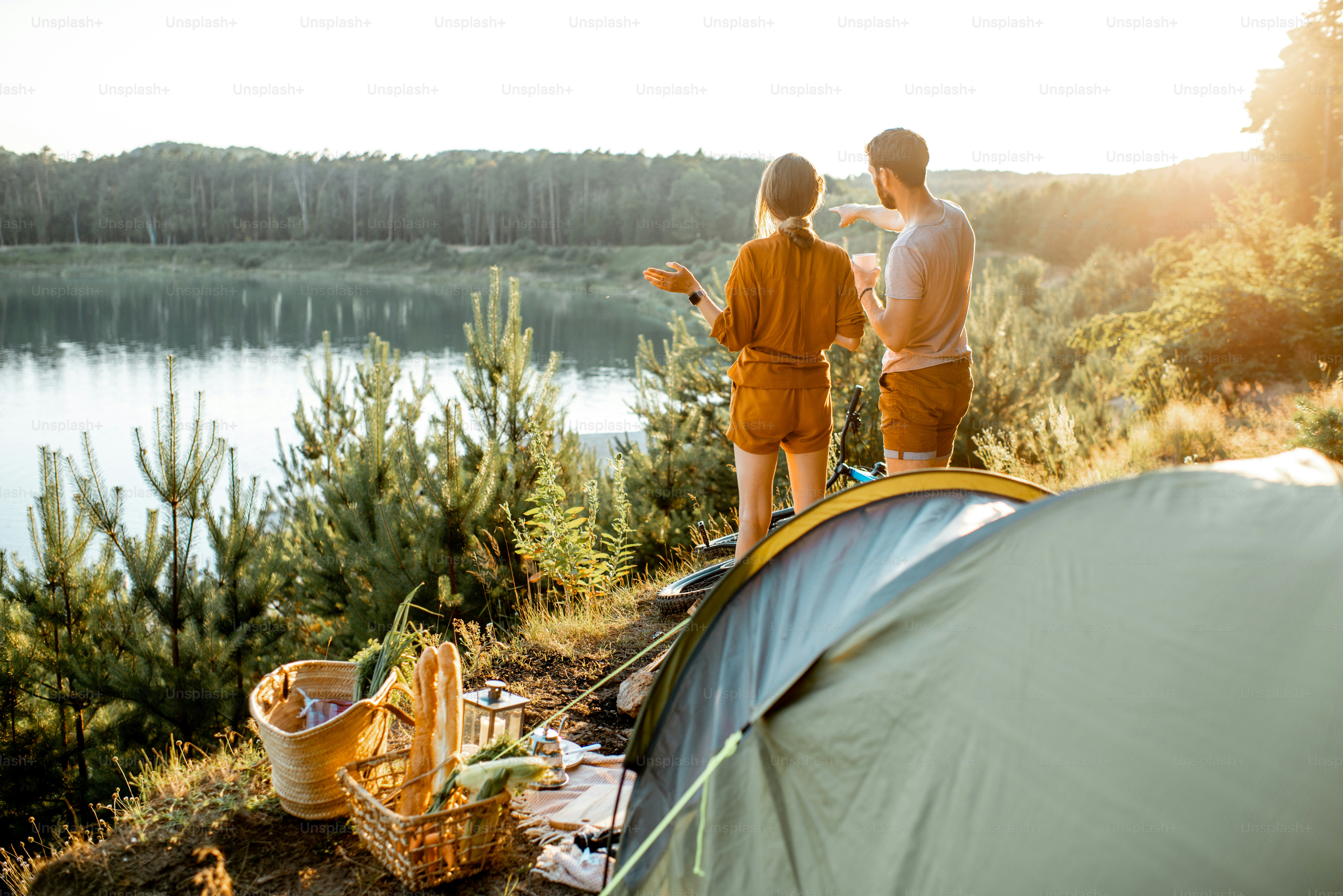 Young couple standing at the campsite, enjoying beautiful view on the lake, while traveling in the mountains on the sunset