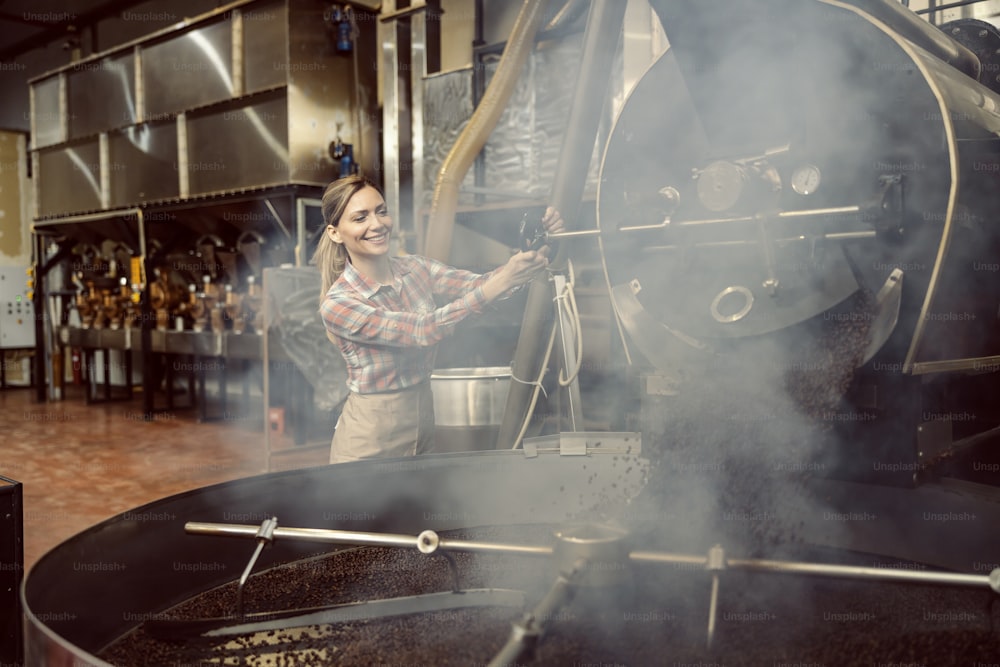 A coffee factory worker operates machine for roasting coffee.