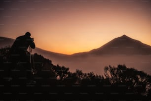 Photographe en action dans le coucher du soleil de paysage avec haute montagne en arrière-plan et des couleurs orange autour des personnes actives sauvages appréciant l’activité de loisirs en plein air