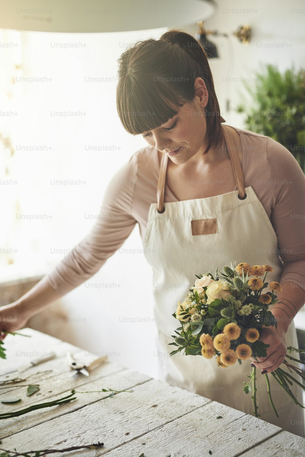 Smiling young female florist standing at a table in her flower shop putting together a bouquet of mixed flowers
