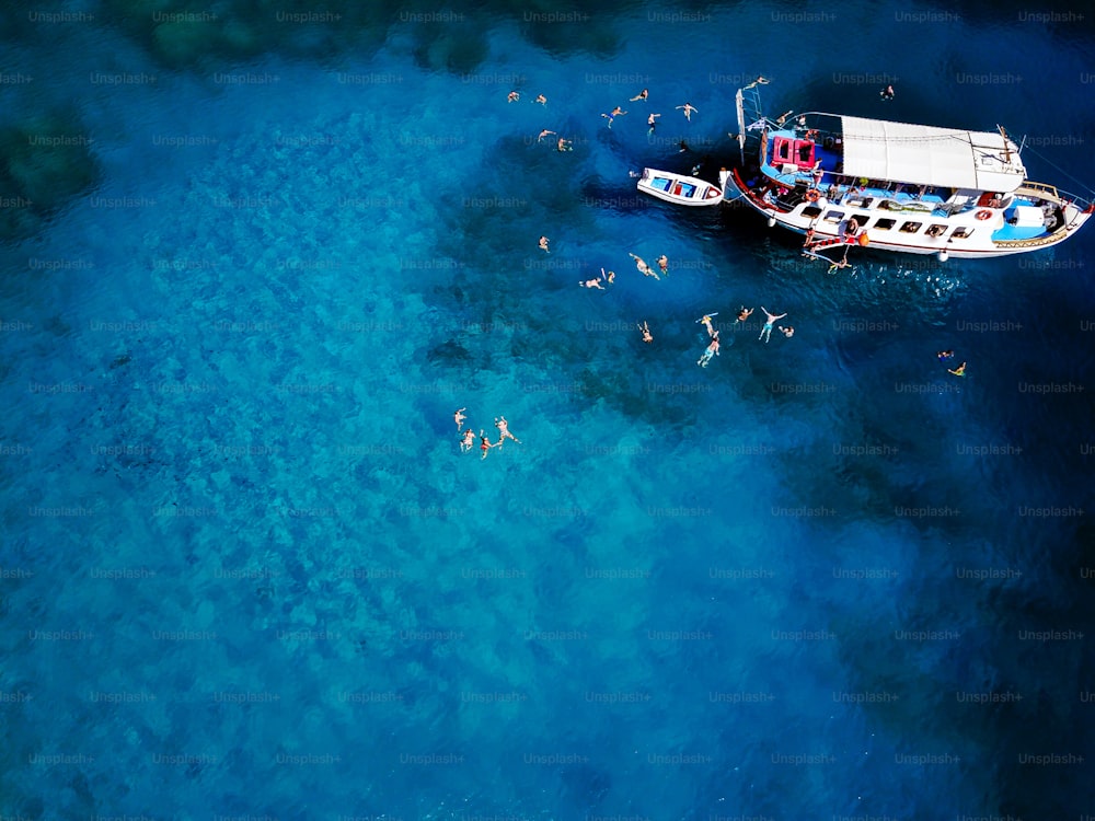 Aerial shot of beautiful blue lagoon at hot summer day with sailing boat. Top view of people are swimming around the boat.