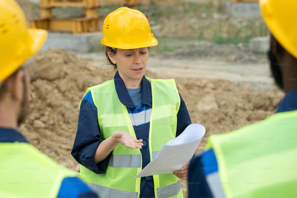 Contemporary engineer with paper standing in front of intercultural male colleagues during discussion