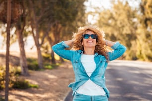 Happy and enjoyed cheerful pretty adult woman in outdoor leisure activity. Portrait of excited female people smiling and having fun walking on the road with trees in background. Pretty lady portrait