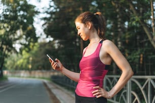 Young slim woman brunette in the sport clothes running and using mobile phone at park on golden hour sunrise time. Health and wellness, fitness lifestyle