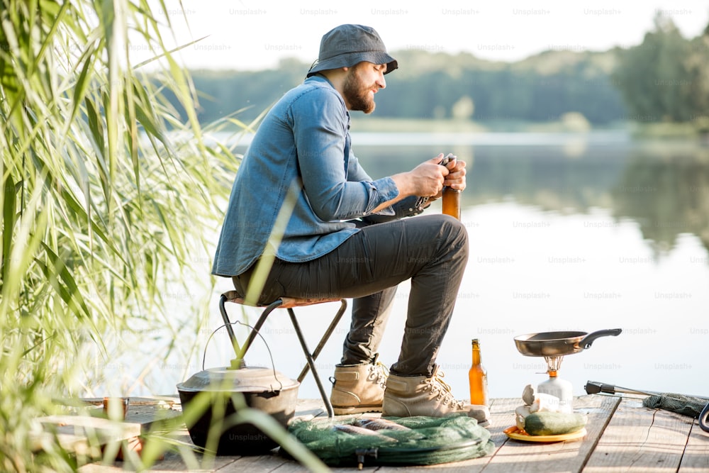 Handsome man relaxing with beer sitting alone during the fishing process on the pier near the lake