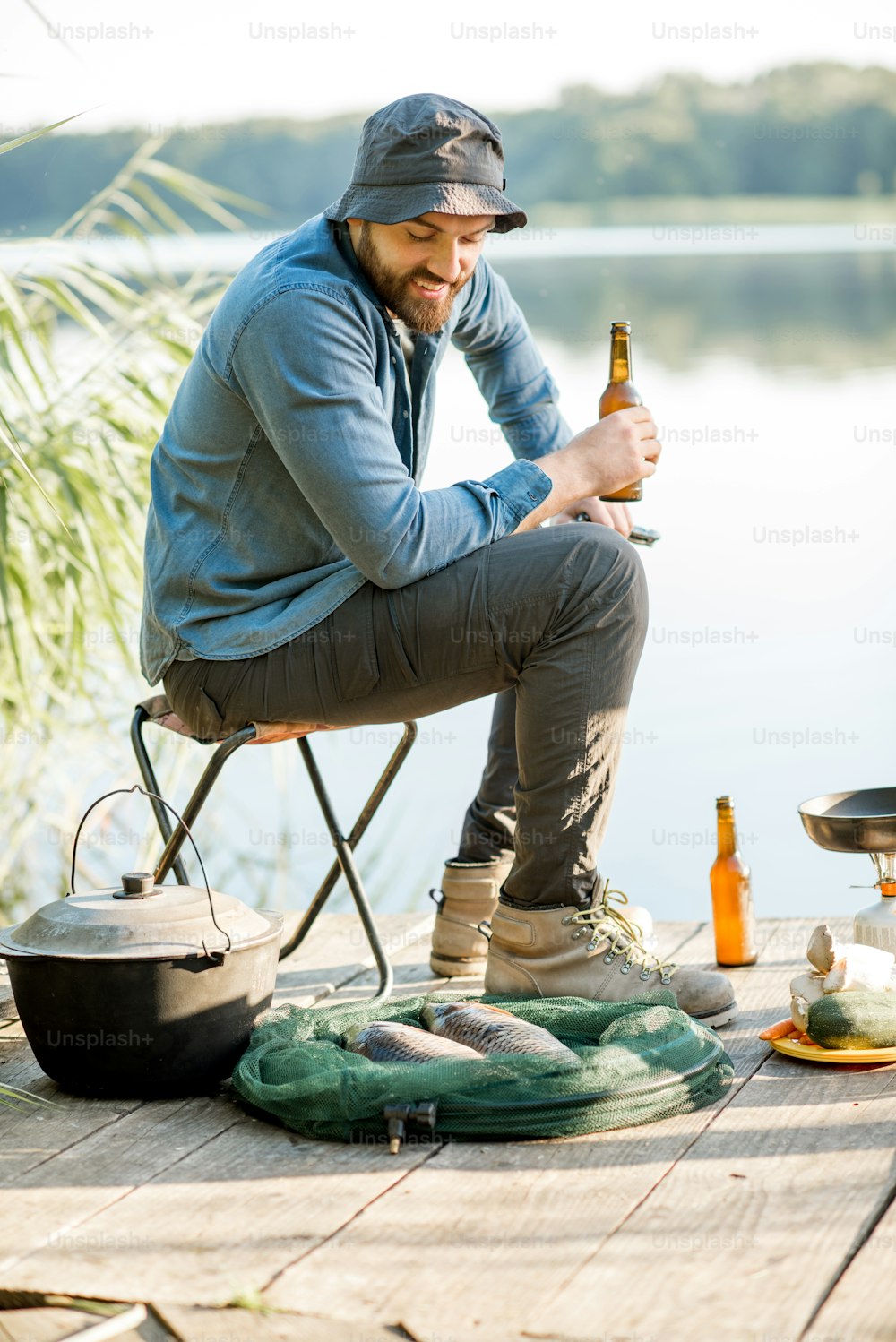 호수 근처 부두에서 낚시 과정에서 혼자 앉아 맥주를 마시며 휴식을 취하는 잘생긴 남자