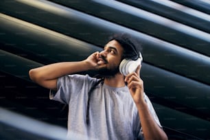 Indian young guy listening music trough the headphones and looking aside.