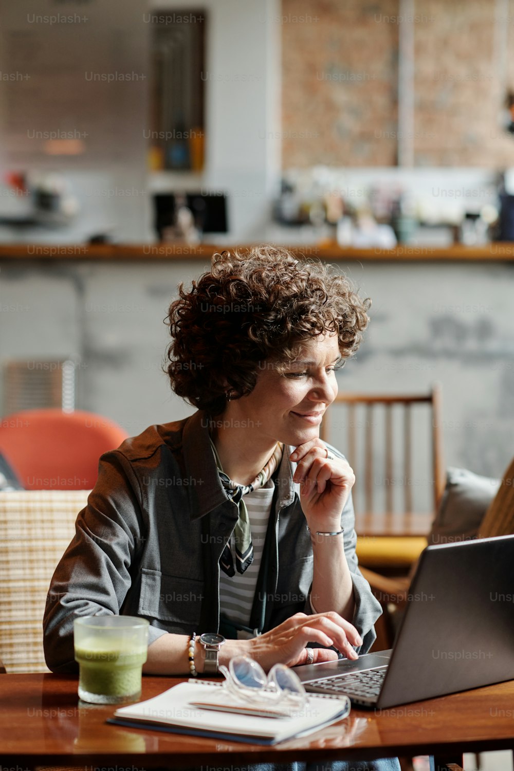 Glückliche Geschäftsfrau oder Freiberuflerin mittleren Alters sitzt am Tisch im Café vor dem Laptop und vernetzt oder kommuniziert im Video-Chat