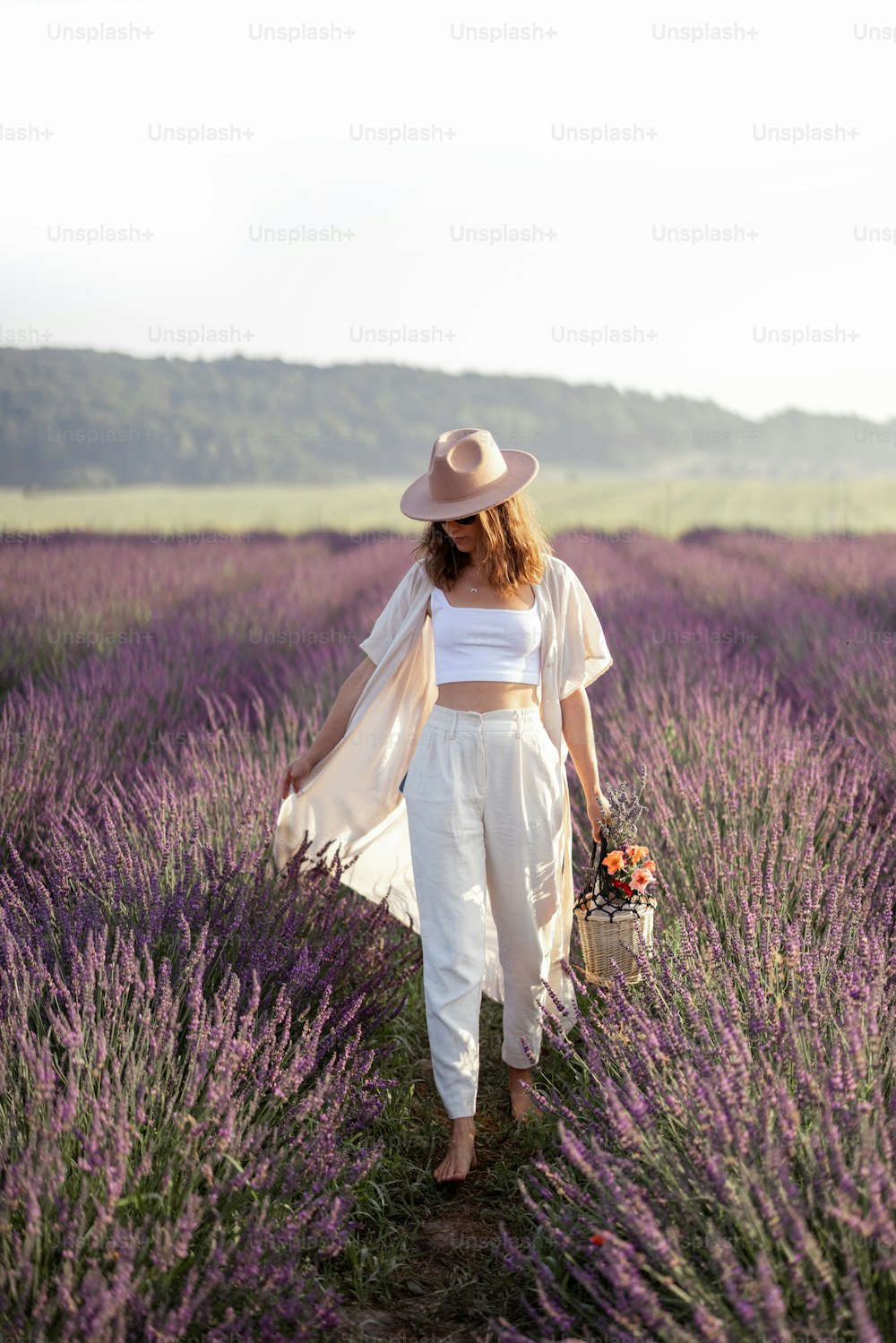 Mujer joven que camina en el campo de lavanda con ramo de flores violetas y disfruta de la belleza de la naturaleza. Calma y concepto consciente. Espacio de copia