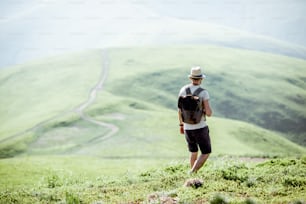 Man hiking with backpack on the beautiful green meadow while traveling in the mountains during the sunny weather