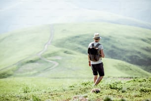 Hombre caminando con mochila en el hermoso prado verde mientras viaja en las montañas durante el clima soleado