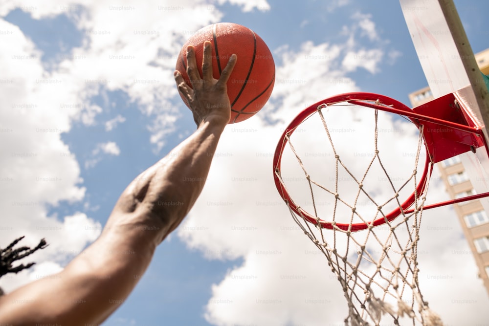 Giocatore di basket africano che lancia la palla nel canestro durante il gioco o l'allenamento con il cielo nuvoloso sopra