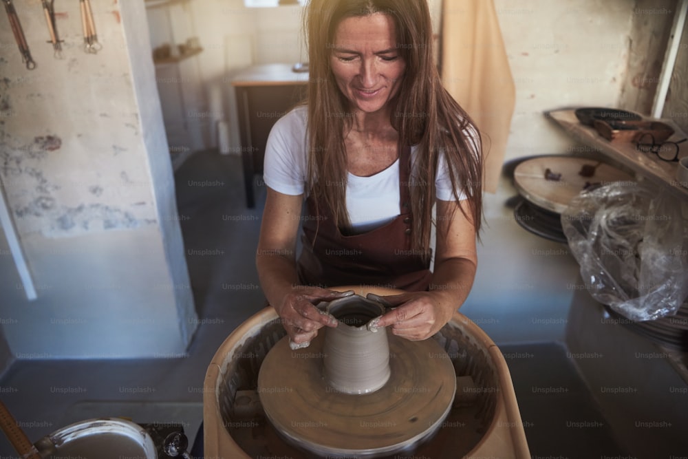 Creative artisan working alone in her ceramic studio shaping wet clay with her hands on a pottery wheel