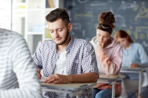 Gruppo di studenti contemporanei seduti da posti individuali e test d'esame di scrittura