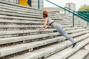 Fit sportswoman listening to music while doing planks on the stairs in an urban part of the city. A sportswoman workout