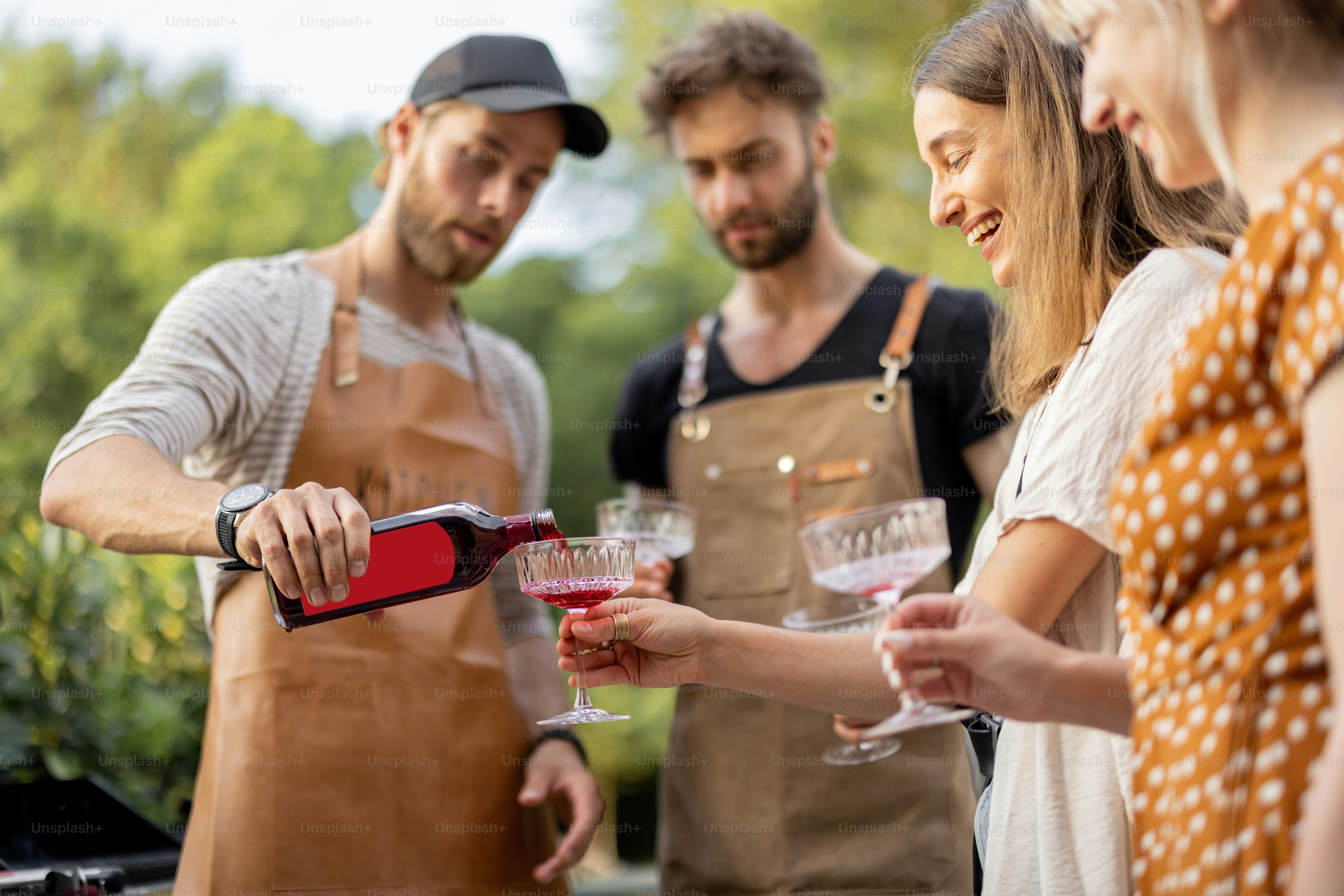 Young people with alcohol drinks at picnic, pouring wine or liqueur ...
