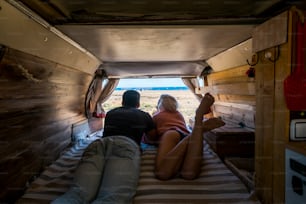 キャンピングカーの駐車場で屋外のビーチと海の前で寝る白人のカップルは、砂浜の上の彼女の窓を楽しんでおり、このまれな選択に満足しています