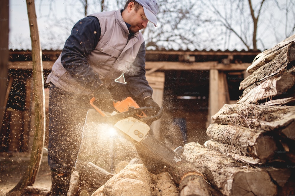 Cortar madera con motosierra en el patio trasero, profesión de leñador.