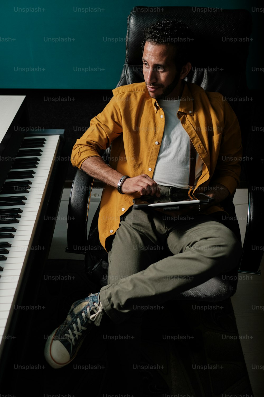 黄色いシャツを着たモロッコ人男性の肖像画は、プロのレコーディングスタジオでタブレットとステージミキサーコントローラーを使用しています