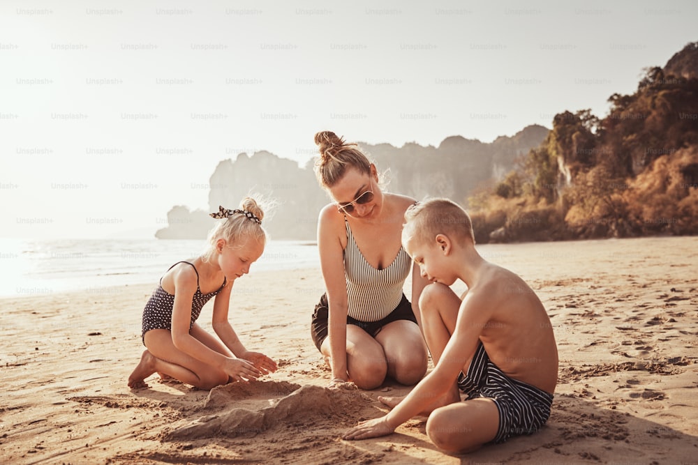 Smiling Mom and her two adorable kids playing together on a sandy beach during their summer vacation
