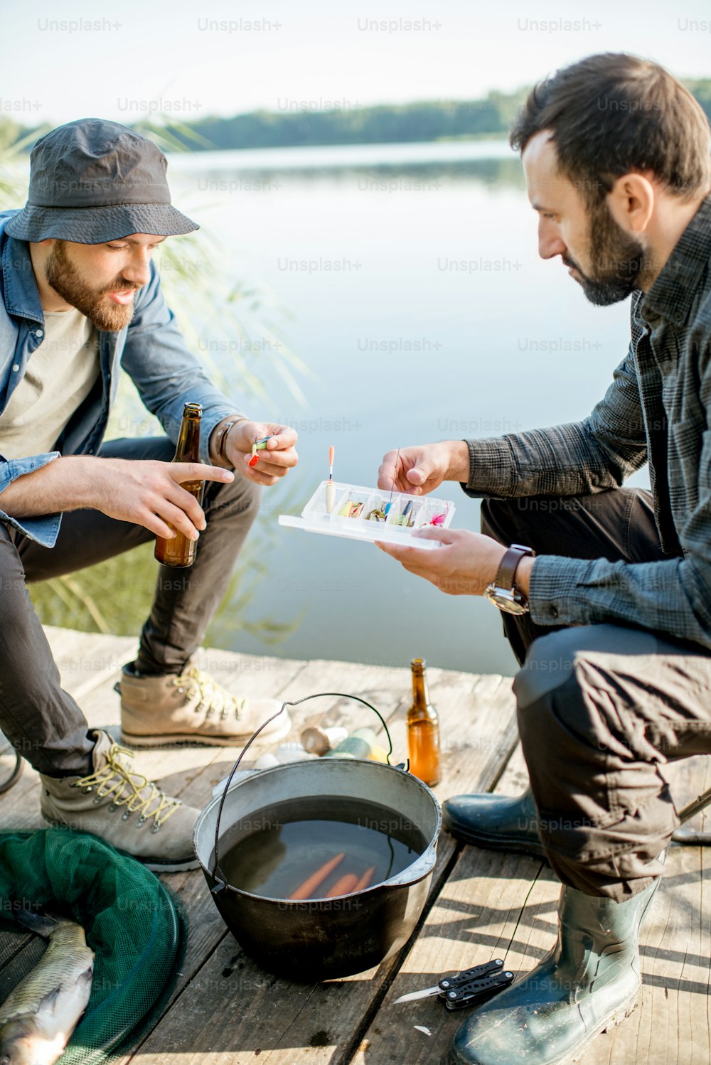 Zwei Fischer sitzen zusammen mit Angelgeräten während des Picknicks in der Nähe des Sees