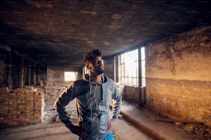 Portrait of focused motivated afro-american young handsome sportive man with earphones standing inside of the abandoned place. Successful young active man portrait.