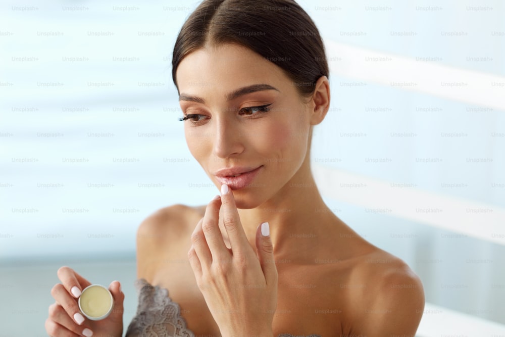 Lips Skin Care. Beautiful Woman With Beauty Face Applying Lip Balsam, Lipbalm On Full Lips. Portrait Of Smiling Female Model With Soft Skin And Natural Nude Makeup Touching Lips. High Resolution