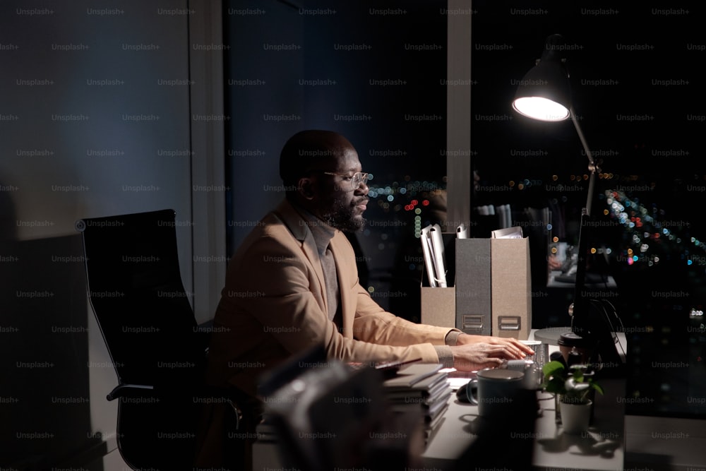 Busy young African man typing on computer keyboard and looking at screen while working late in office