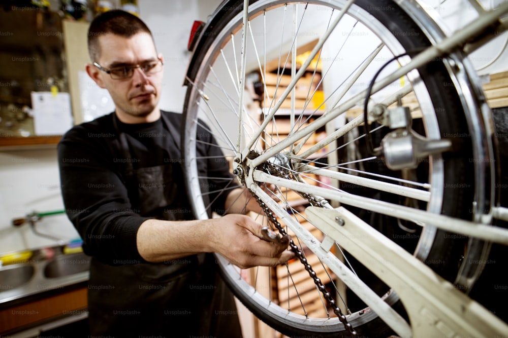 Hombre enfocado profesional que verifica si la cadena de la rueda de la bicicleta está bien colocada.