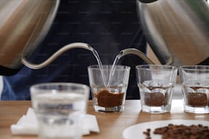 Close up of male barista pouting boiling water into glass cups with ground coffee from two kettles, brewing fresh coffee for cupping exam