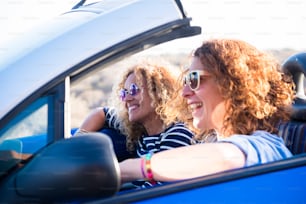 Couple of curly cheerful woman smiling and having fun together enjoying the travel vacation driving the car - people on the move in convertible vehicle in sunny day of summer