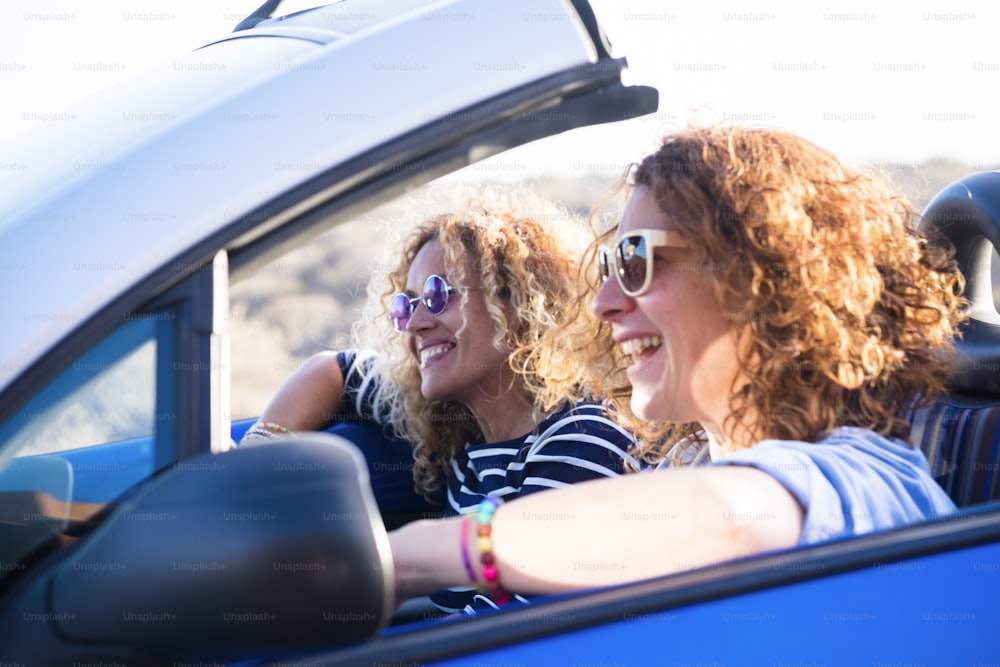 Couple of curly cheerful woman smiling and having fun together enjoying the travel vacation driving the car - people on the move in convertible vehicle in sunny day of summer