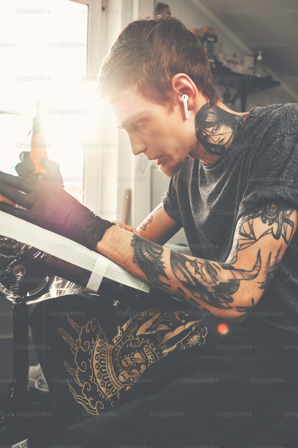 A young guy, beats a tattoo on the hand of the girl in a tattoo parlor, rotary tattoo machine, black ink, lens flare