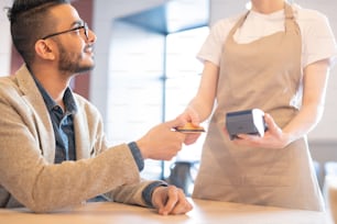 Young elegant businessman giving plastic credit card to waitress in cafe while going to pay for lunch
