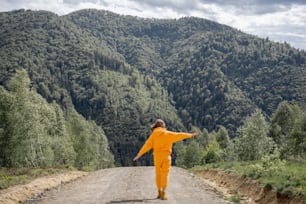 Jovem em terno esportivo laranja caminha na estrada nas montanhas. Conceito de viajar nas montanhas