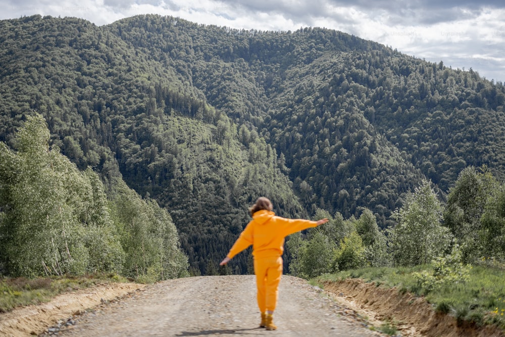 Young person in orange sports suit walks on road in the mountains. Concept of traveling in the mountains