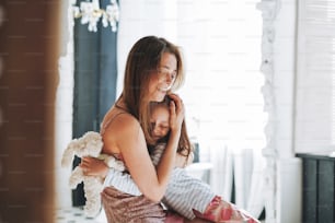 Young mother woman with long hair with little tween girl daughter in pajamas having fun in the morning at home