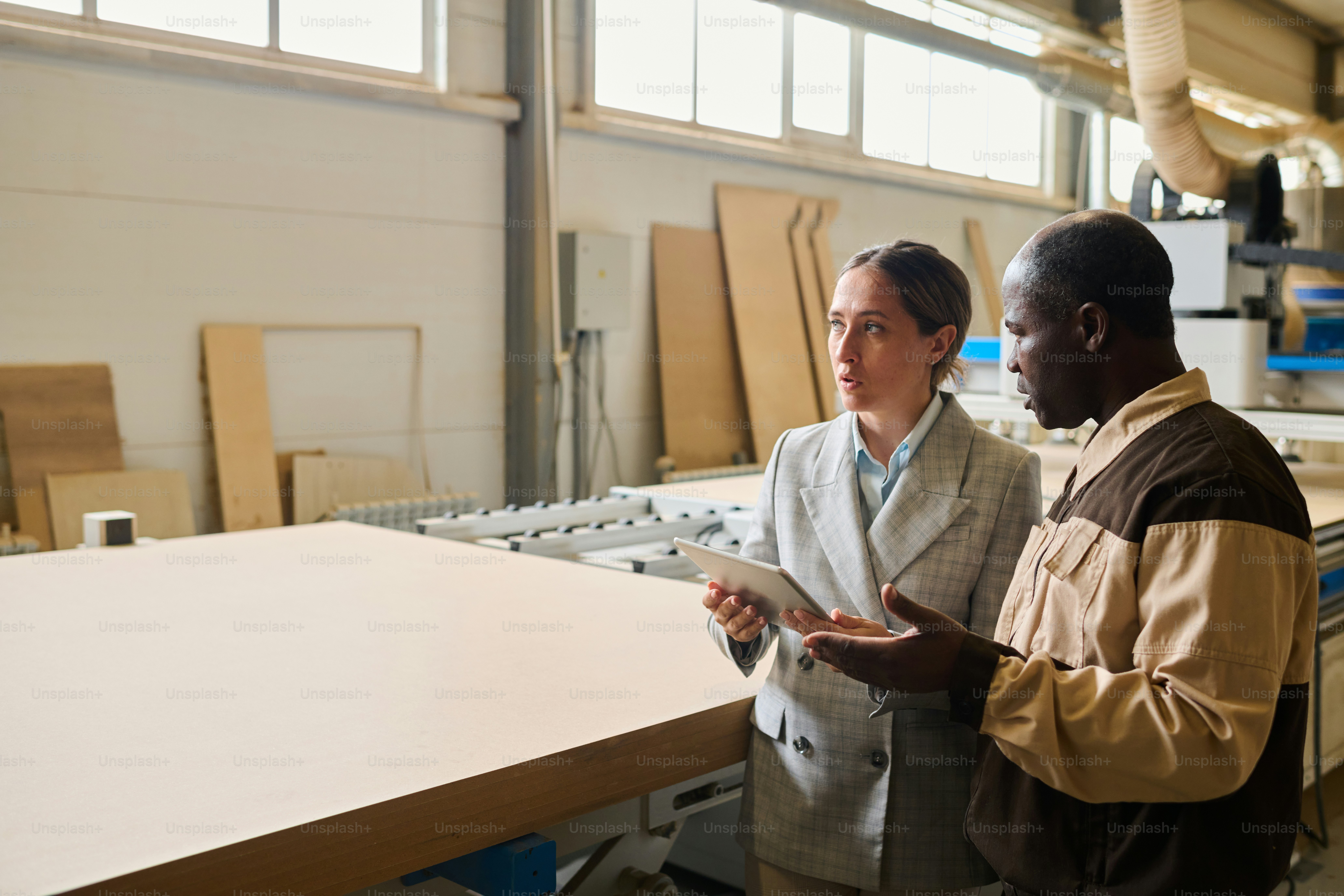 Female engineer using tablet pc and discussing work of machine with foreman at factory