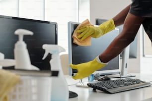 Gloved hands of young African American man with duster wiping computer screen while standing by workplace of office manager