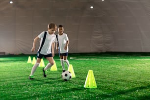 Deux petits joueurs de football courant après le ballon tout en s’entraînant sur un terrain avec des cônes