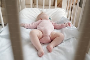Sweet infant girl in pink clothes resting in her cradle inside bedroom