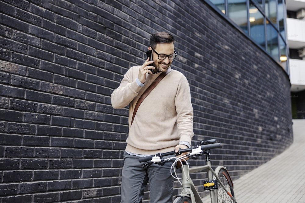 Um empresário casual empurrando bicicleta e conversando por telefone na rua do centro da cidade.