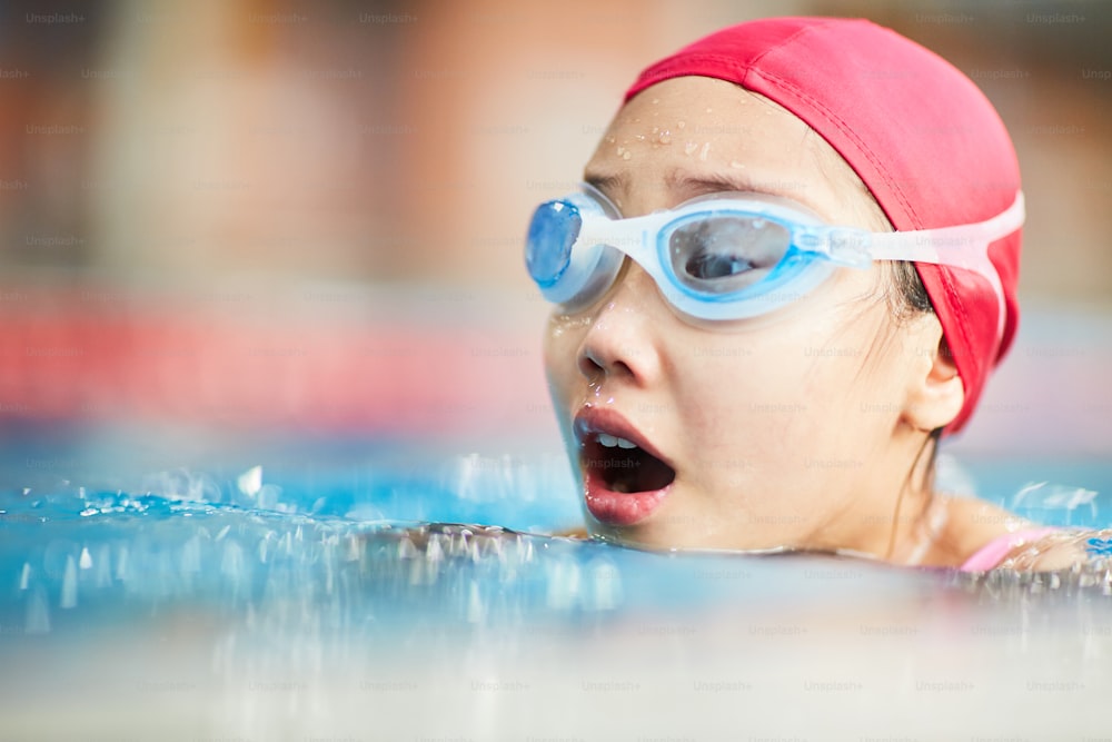 수영 모자를 쓰고 고글을 쓴 작은 수영 선수는 수영하는 동안 물 위에서 숨을 쉬고 있습니다.