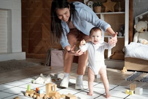 Joyful young mother spending spare time at home having fun with her baby daughter learning to walk